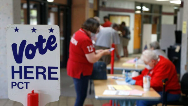 Photo of a polling place with two people and a sign that reads "vote here"
