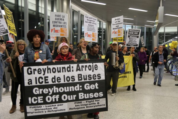 Person holding a protest sign in a Greyhound Bus Terminal