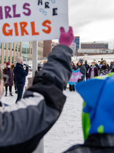 Image of someone holding a sign that says, "Trans girls are girls."