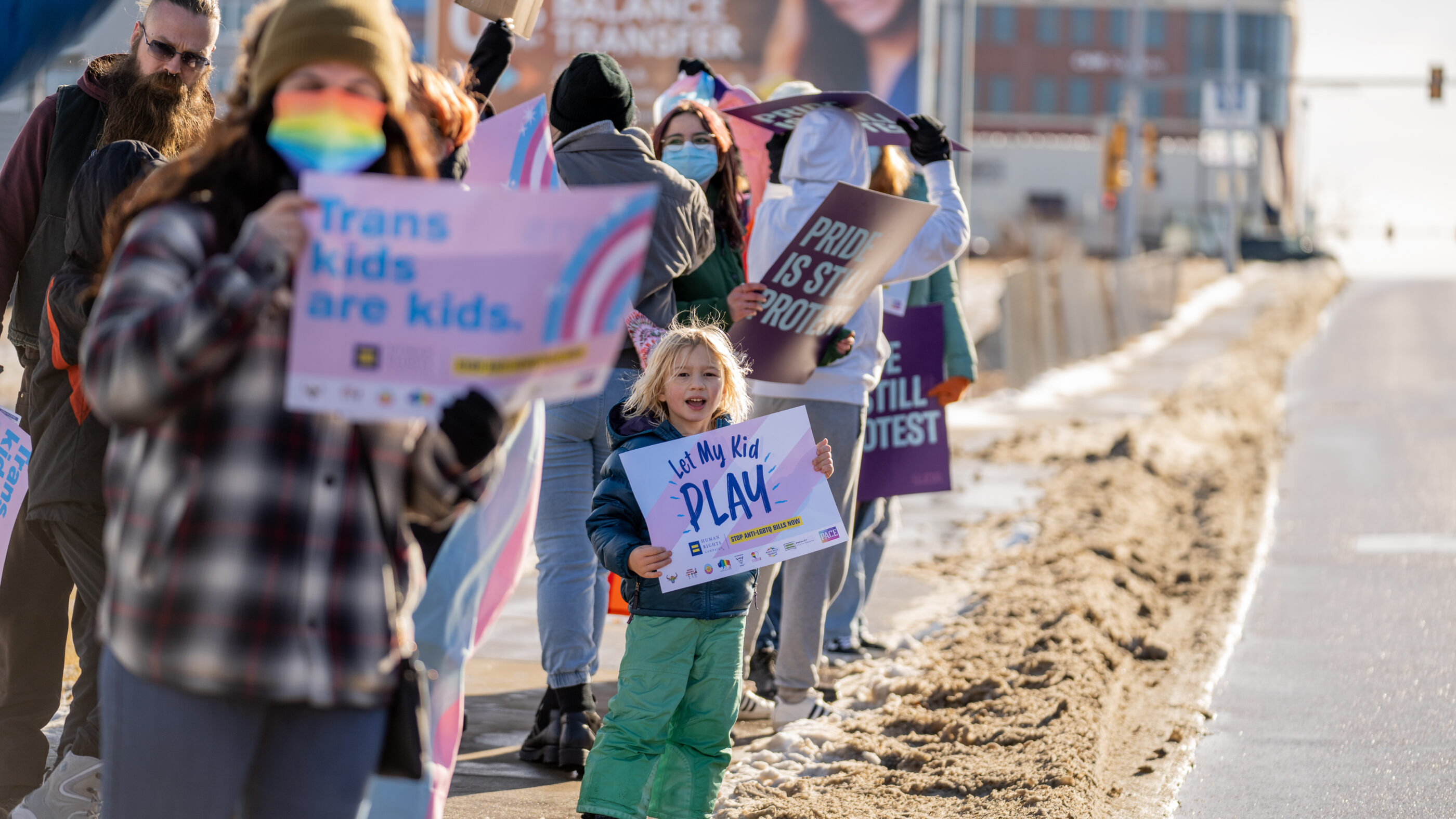 Image of a kid holding a sign that says, "Let trans kids play"