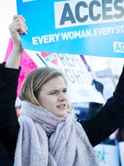 photo of a woman holding up a sign that reads, "every woman every state"