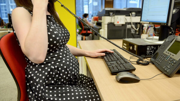 A pregnant worker using an office phone while typing on a keyboard.