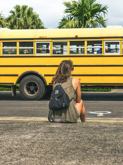 Person in front of a school bus with a backpack.