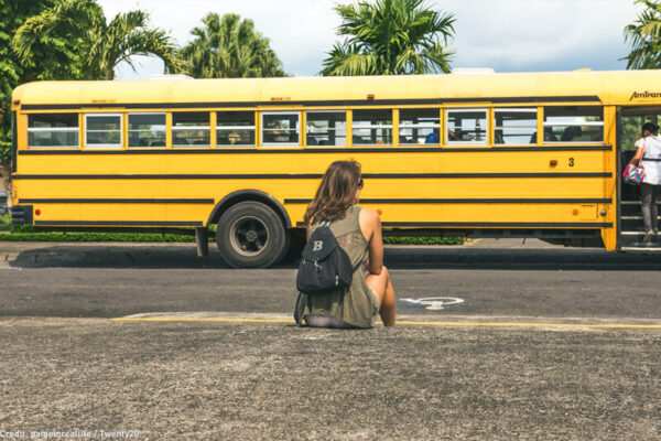 Person in front of a school bus with a backpack.
