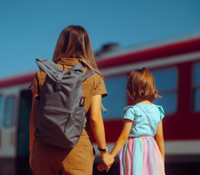 An image of a woman wearing a backpack holding the hand of a child.