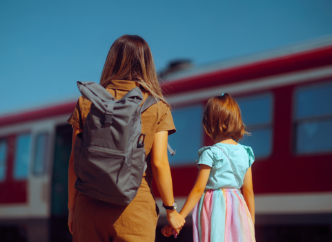 An image of a woman wearing a backpack holding the hand of a child.