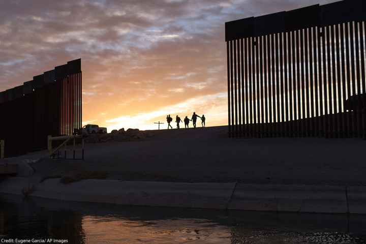 A pair of migrant families at the border wall between the United States and Mexico.
