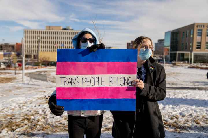 Image of two people holding a sign that reads, "trans people belong."
