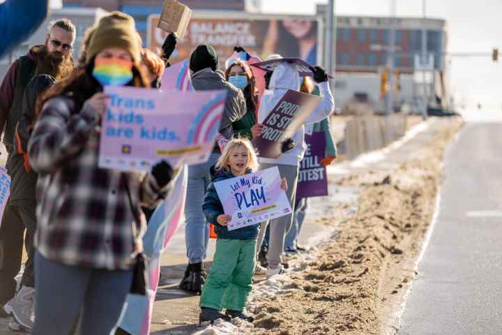 Image of a kid holding a sign that says, "Let trans kids play" Image of a kid holding a sign that says, "Let trans kids play"