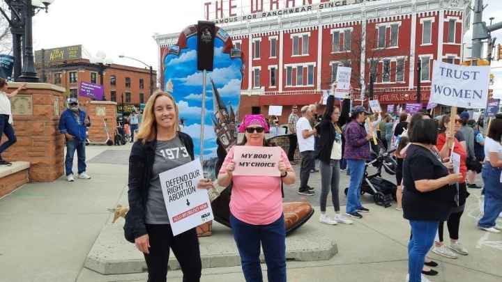 Image of two protesters at a rally holding signs that support abortion access.