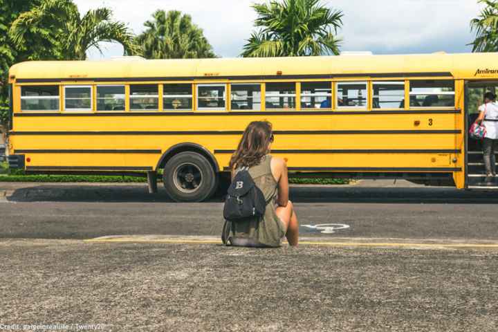 Person in front of a school bus with a backpack. 