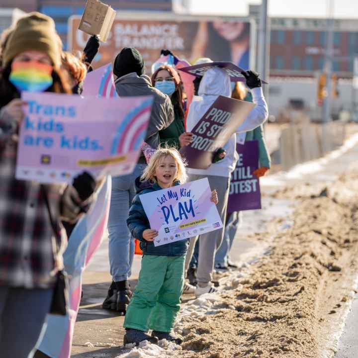 Image of a kid holding a sign that says, "Let trans kids play" Image of a kid holding a sign that says, "Let trans kids play"