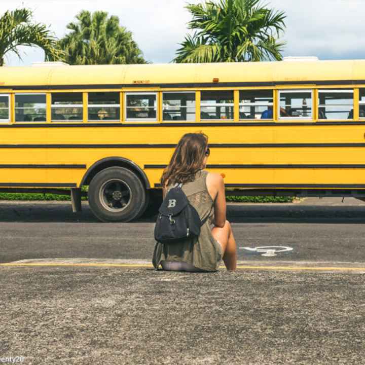 Person in front of a school bus with a backpack. 